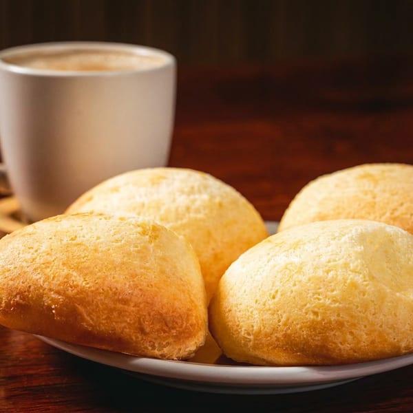 A plate of four golden buns and a coffee mug on a dark wooden table.