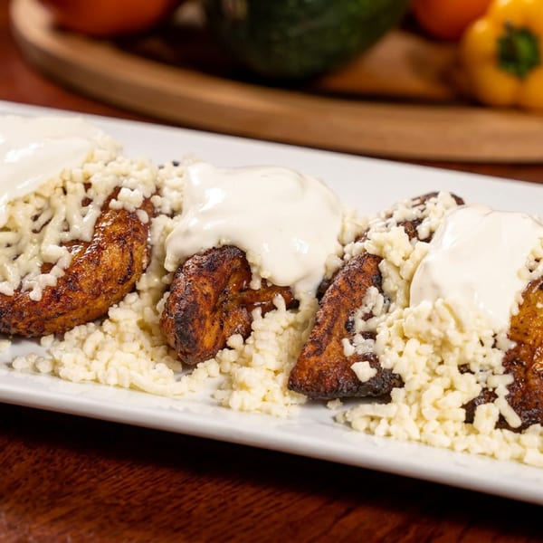 Three fried plantains topped with white cream and crumbled cheese on a white plate.