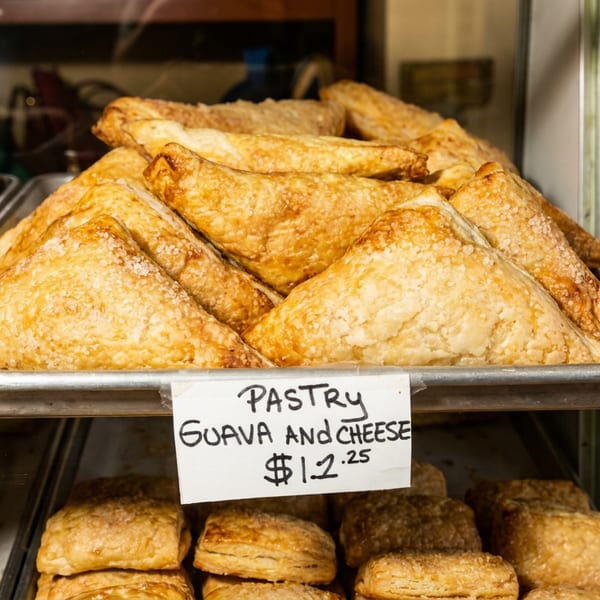 Golden brown guava and cheese pastries on a tray with a $1.25 price tag.