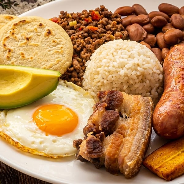 Hearty Colombian bandeja paisa featuring rice, beans, meats, egg, avocado, and fried plantains.